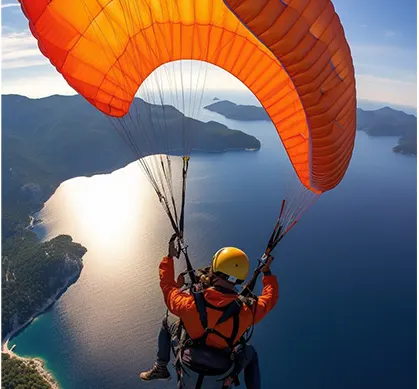 Paraglider soaring over a lake with mountains — vibrant orange parachute in flight.